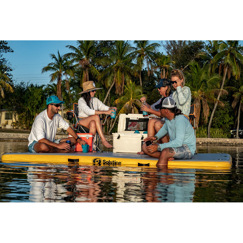 Group of friends sitting on Solstice inflatable floating dock with cooler and drinks, enjoying lake day on the water