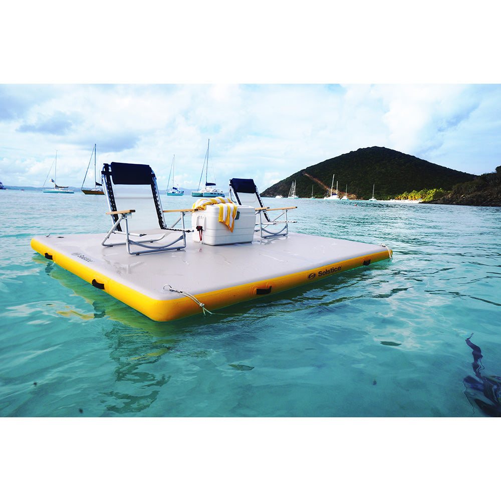 Solstice inflatable dock platform with lounge chairs and cooler floating on clear blue water with sailboats in the background