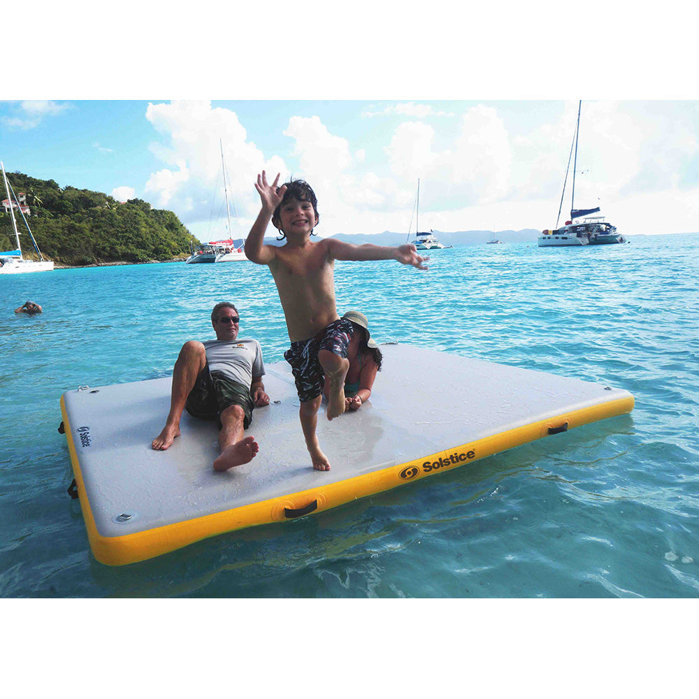 Family enjoying a Solstice inflatable dock platform on the water, child jumping while adults relax in the sun