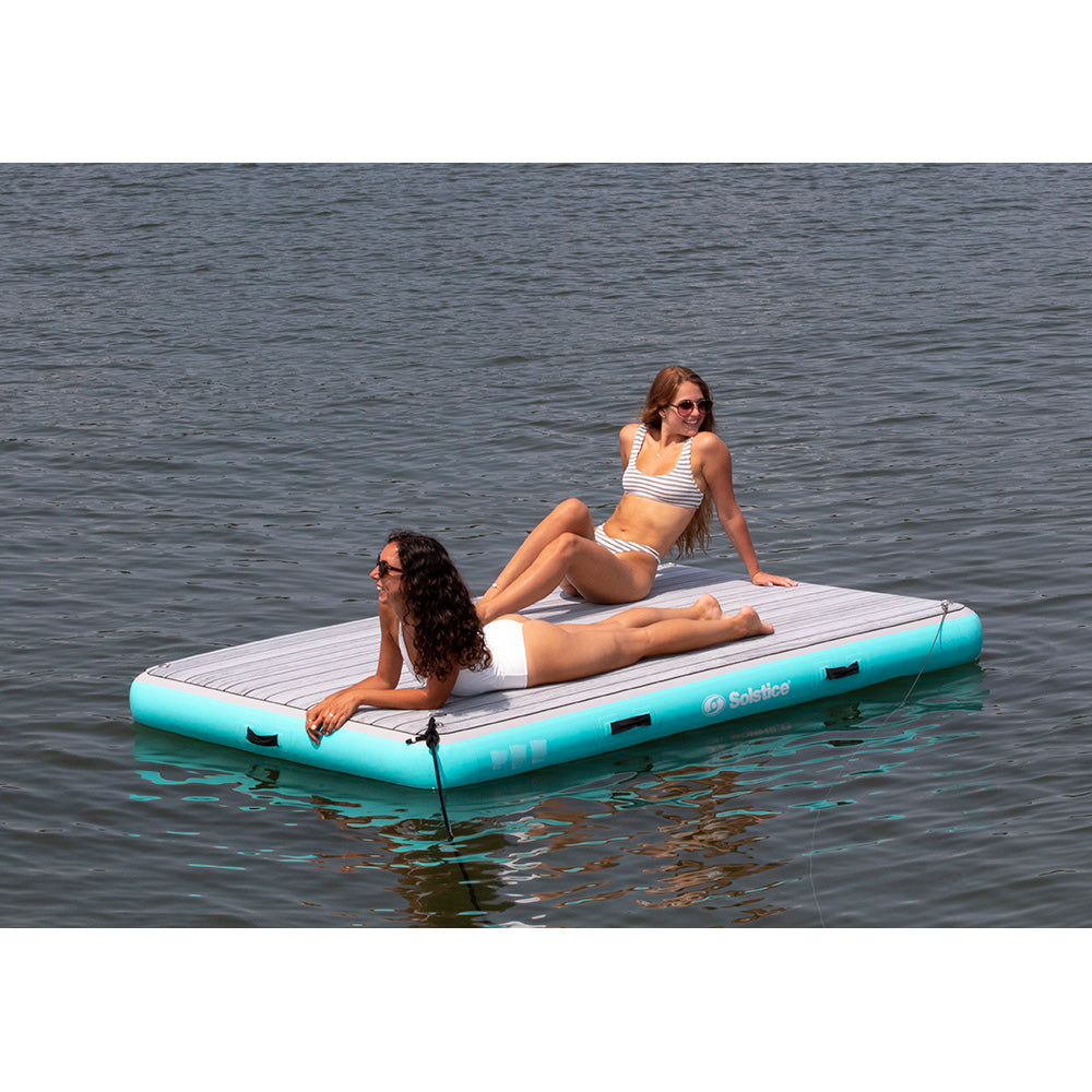 Two women relaxing on a Solstice inflatable dock platform floating on a calm lake