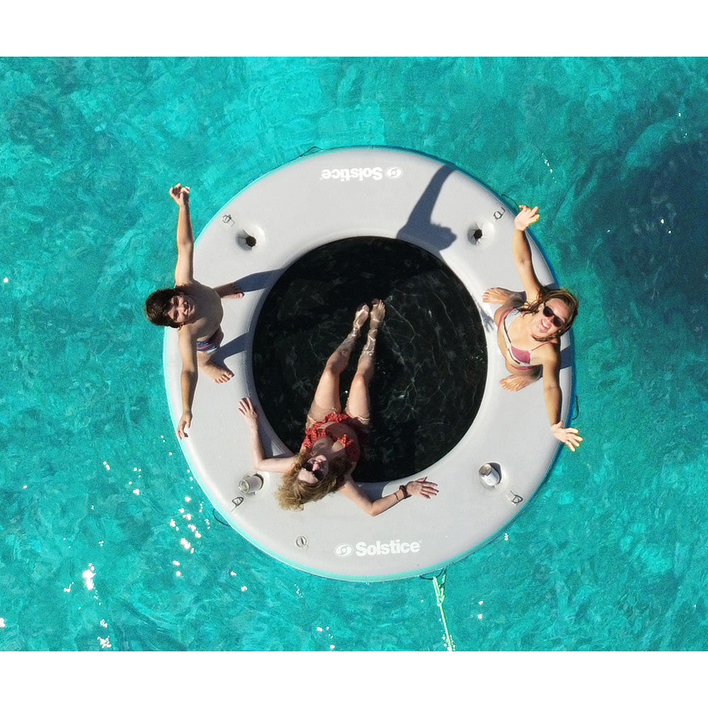 “Solstice inflatable floating lounge with swim center hole and people relaxing on turquoise water”