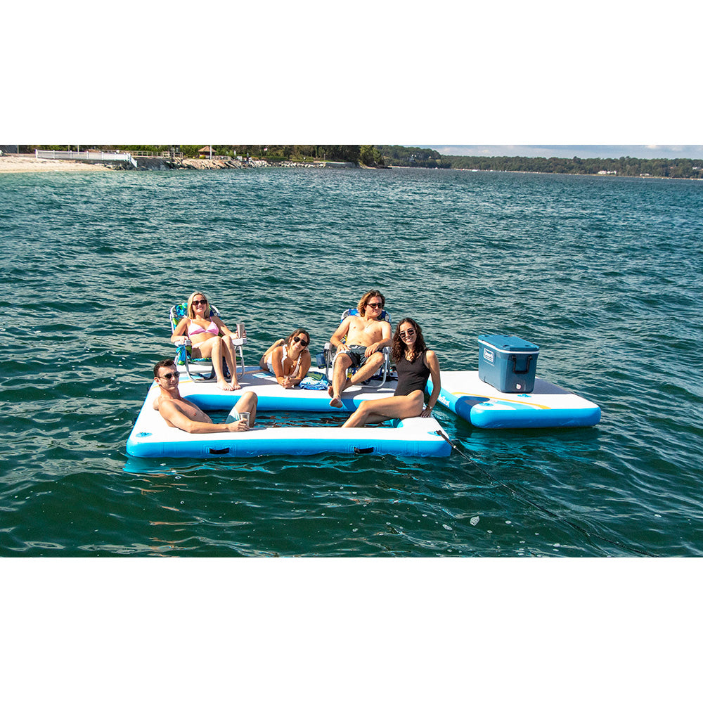 “Group of friends lounging on two blue and white Solstice inflatable docks connected together with a cooler on a lake”