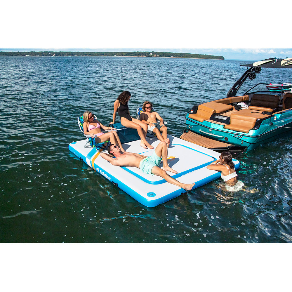 “Group relaxing on a blue and white Solstice inflatable dock platform tied to a boat on a lake”