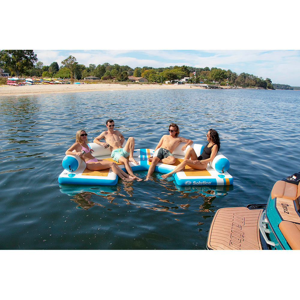“Four adults relaxing on Solstice inflatable lounge docks connected together on the lake near a boat.”